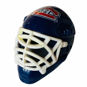 May include: A blue and white plastic hockey goalie mask with a white cage and a red and white logo on the front. The logo is a stylised letter "C" with a "B" inside it.