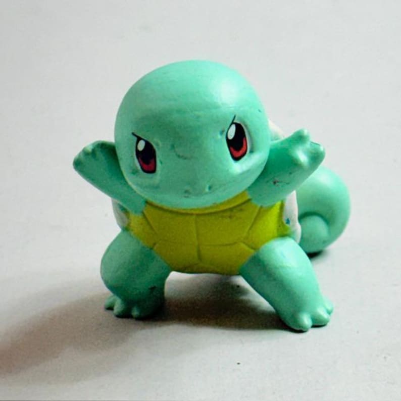 Puede incluir: Una peque&ntilde;a figura de Squirtle turquesa con caparaz&oacute;n amarillo. La figura tiene ojos rojos y est&aacute; posando con los brazos extendidos. Este juguete coleccionable es de la franquicia Pok&eacute;mon.