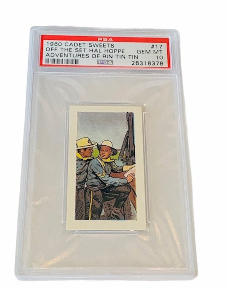 Pode incluir: Um cart&atilde;o de cole&ccedil;&atilde;o de 1960 da Cadet Sweets, classificado pela PSA. O cart&atilde;o mostra dois homens em uniformes militares, com o texto "#17 OFF THE SET HAL HOPPE GEM MT ADVENTURES OF RIN TIN TIN 10 26318378" impresso no cart&atilde;o.