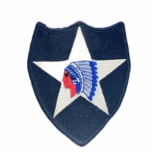 May include: A navy blue patch with a white star and a Native American profile in red, white, and blue. The patch has a shield shape and is likely an emblem or insignia.