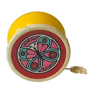 May include: A vintage yellow and white yo-yo featuring a butterfly design. The yo-yo has a red border with the words "BUTTERFLY" and "DUNCAN". The butterfly is pink, teal, and black.