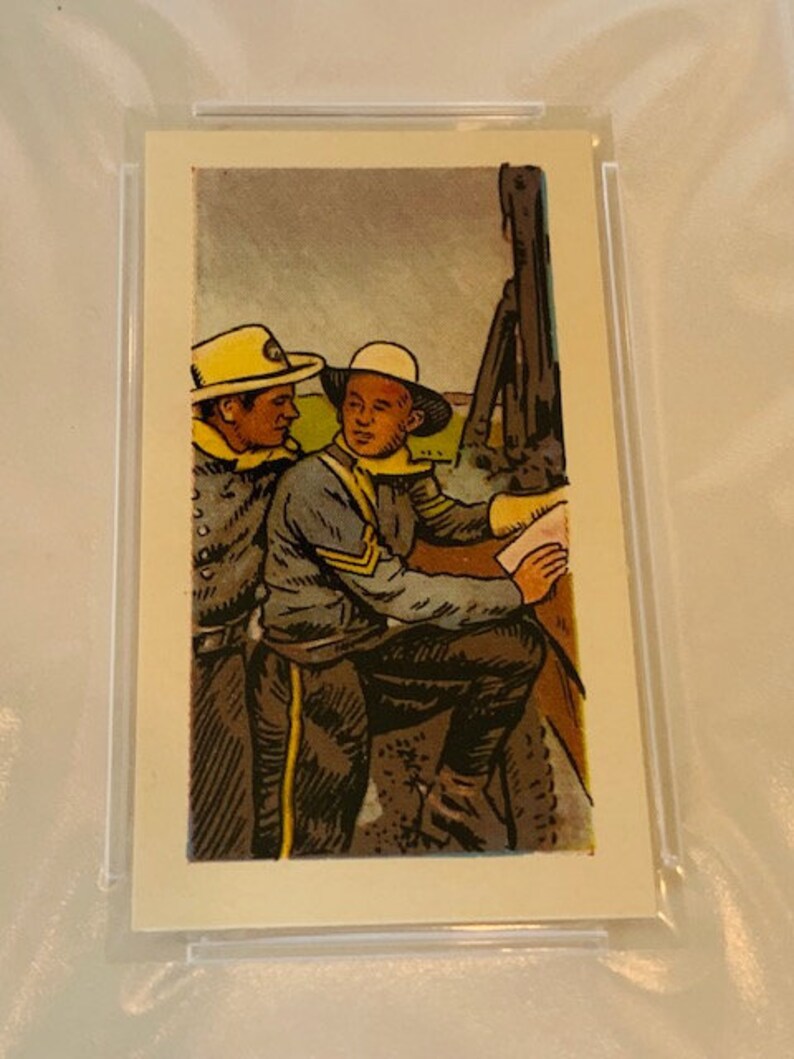 Pode incluir: Dois homens com uniformes militares, um com um chap&eacute;u amarelo e o outro com um chap&eacute;u marrom, est&atilde;o de p&eacute; ao lado de um canh&atilde;o grande. Os homens se olham e parecem estar falando.