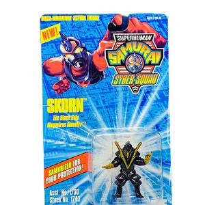 Può includere: Una action figure nera e gialla di Skorn, il mostro Megavirus del buco nero della linea di giocattoli Superhuman Samurai Syber-Squad. La figura è confezionata in una blister blu e gialla con il nome del personaggio e una descrizione dei suoi poteri. La confezione include anche il testo "Samurized for your protection!" e i numeri di prodotto 1730 e 1743.