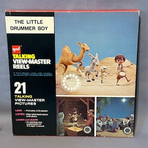 May include: Vintage "The Little Drummer Boy" GAF Talking View-Master Reels box set. The box features illustrations of the nativity scene, including a camel, donkey, and drummer boy. The box includes 21 talking view-master pictures.