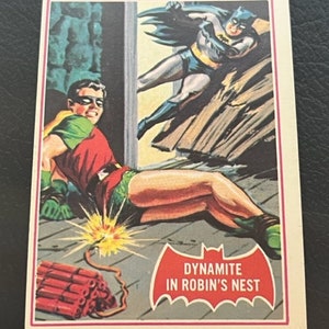 Może przedstawiać: Winietkowa karta kolekcjonerska z komiksu z Batmanem i Robinem. Karta przedstawia Robina leżącego na ziemi z zapaloną lontem obok niego. Batman jest w tle, lecąc, aby uratować Robina. Karta zawiera tekst "Dynamite in Robin's Nest".