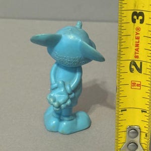Pu&ograve; includere: Una statuetta di plastica blu di un topo dei cartoni animati che tiene un piccolo oggetto. La statuetta &egrave; alta circa 5 cm e ha le parole "Walt Disney Productions Hong Kong" stampate sul retro.