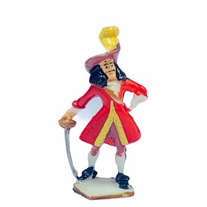 May include: A small plastic figurine of Captain Hook from Peter Pan. He is wearing a red and gold coat, black trousers, and a black hat with a yellow feather. He is holding a sword in his right hand and has a stern expression on his face.