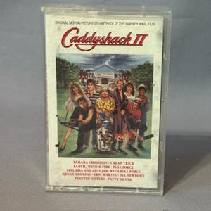 May include: A vintage cassette tape for the movie "Caddyshack II" in a clear plastic case. The cover features a group of people and the movie title in red. The soundtrack includes songs by Tamara Champlin, Cheap Trick, and others.