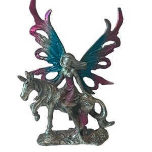 May include: A pewter figurine of a fairy riding a unicorn. The fairy has pink and blue wings and a purple dress. The unicorn is silver.