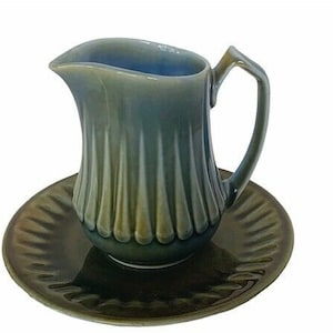 May include: A green and blue ceramic creamer with a fluted design and a handle. The creamer is sitting on a matching saucer.