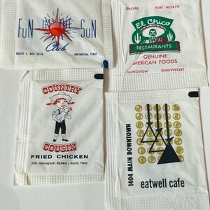 May include: Four vintage paper packets with different business logos. The first packet is white with a red and blue logo that says "Fun in the Sun Club" with a star and a red circle. The second packet is white with a green logo that says "El Chico Restaurants" with a fork and knife and a man with a sombrero. The third packet is white with a red and blue logo that says "Country Cousin Fried Chicken". The fourth packet is white with a black and gold logo that says "eatwell cafe" with a design of three triangles and circles.