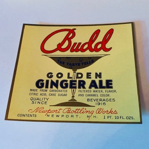 Puede incluir: Una etiqueta vintage para el Golden Ginger Ale de Budd. La etiqueta es amarilla con un borde dorado y presenta un logotipo en escritura cursiva roja con el texto "Budd" y "The Taste Tells". La etiqueta también incluye el texto "Golden Ginger Ale", "Hecho de ácido cítrico carbonatado, azúcar de caña", "Agua filtrada, sabor y color caramelo", "Calidad desde", "Bebidas 1916", "Newport Bottling Works", "Contenido Newport, N.H. 1 Pt. 10 Fl. Ozs."