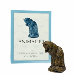 May include: A bronze figurine of a cat grooming itself. The figurine is part of The Curio Cabinet Cats Collection by Animalier.
