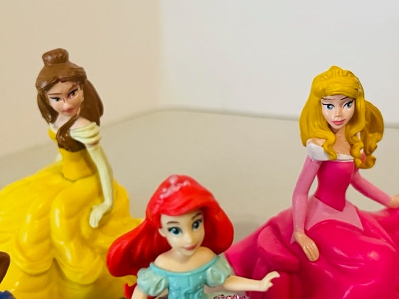 May include: Three Disney princess figurines: Belle in a yellow dress, Ariel in a blue dress, and Aurora in a pink dress.