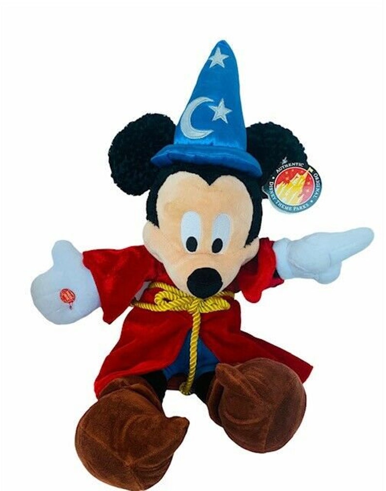 May include: A plush Mickey Mouse wearing a blue wizard hat with a silver crescent moon and star. He is wearing a red robe with gold rope trim and brown shoes. The plush is labeled "Authentic Disney Theme Parks Merchandise."