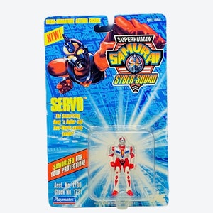 Può includere: Una action figure rossa, bianca e blu di un supereroe chiamato Servo di Superhuman Samurai Syber-Squad. La figura è confezionata in una blister di plastica con sfondo blu e bianco. La confezione include il testo "Superhuman Samurai Syber-Squad", "Servo", "Samurized for your protection!" e "Asst. No. 1730 Stock No. 1731 Playmates".