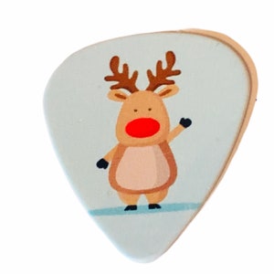 May include: A light blue guitar pick with a cartoon reindeer wearing a red nose. The reindeer is brown with antlers and is standing on a white background.
