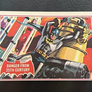 Könnte beinhalten: Eine Vintage-Comic-Sammelkarte mit Batman in einer futuristischen Umgebung. Die Karte hat einen roten Hintergrund mit dem Text "Danger from 25th Century" in Weiß. Batman ist in einem dunkelblauen Anzug mit einem gelben Gürtel dargestellt, der gegen einen Roboterfeind kämpft.