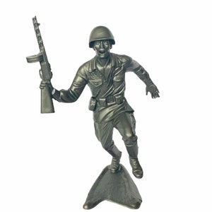 Peut inclure: Une figurine de soldat en plastique gris courant avec un fusil à la main. Le soldat porte un casque et un uniforme. La figurine est debout sur une base en plastique gris.