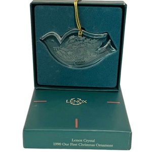 May include: A green box with a clear glass dove ornament inside. The box has the words "Lenox Crystal 1990 Our First Christmas Ornament" printed on the front.