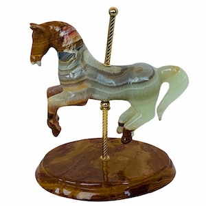 May include: A hand-carved onyx carousel horse figurine with a brown, green and white striped pattern. The horse is mounted on a wooden base with a gold-coloured metal pole.