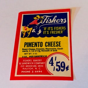 May include: A vintage advertisement for Fishers Bakery & Sandwich Company, featuring a cartoon illustration of a woman fishing. The text reads "Fishers "IF IT'S FISHERS IT'S FRESHER" PIMENTO CHEESE Bread, Cheese, Pimentos, Mayonnaise, Condiments, 1/10 of 1% Benzoate of Soda NET WT. 3 OZ. 3 OZ. PER SANDWICH FISHERS BAKERY & SANDWICH COMPANY 1519 BROOKSIDE DRIVE RALEIGH, N. C. PHONE 2-6494 4'59¢"