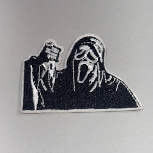 Könnte beinhalten: Schwarz-weißer, gestickter Aufnäher mit der ikonischen Scream-Maske, die ein Messer hält. Der Aufnäher hat eine rechteckige Form mit schwarzem Hintergrund und weißen Details, ideal für Jacken, Taschen oder andere Textilien.