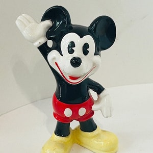 May include: A black and white ceramic figurine of Mickey Mouse wearing red shorts with white polka dots. He is waving with his right hand and his left hand is on his hip. He has a big smile on his face.