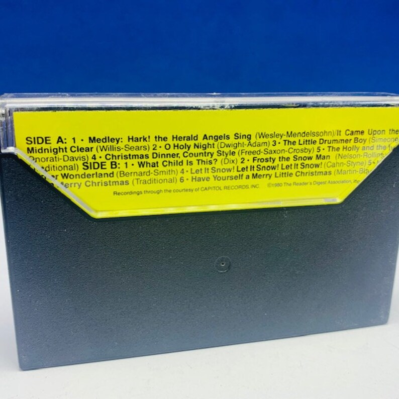 May include: A yellow cassette tape with the title "Christmas Dinner, Country Style" printed on it. The tape is labelled with the song titles "Hark! The Herald Angels Sing", "O Holy Night", "The Little Drummer Boy", "Midnight Clear", "What Child Is This?", "Frosty the Snowman", "Let It Snow! Let It Snow! Let It Snow!" and "Have Yourself a Merry Little Christmas".
