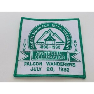 May include: Green Mountain Falls, Colorado Centennial Celebration patch with a white background and green text. The patch features a green mountain range with a pagoda-style building in the center. The text reads "Green Mountain Falls, Colorado", "1890-1990", "Centennial Celebration", "Falcon Wanderers", and "July 28, 1990".