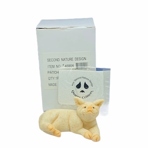 Peut inclure: Une figurine de cochon en céramique blanche couchée avec une expression joyeuse. Le cochon fait partie de la collection Quarry Critters de Second Nature Design. La figurine est emballée dans une boîte blanche avec le logo de l'entreprise et des informations sur le produit.