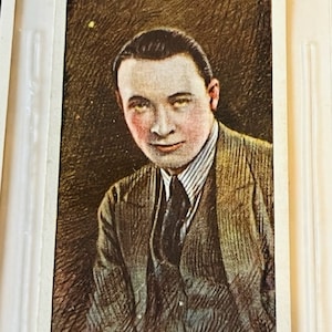 May include: A vintage cigarette card featuring a black and white portrait of a man with a dark suit and a striped tie. The card has the text "WILLS'S CIGARETTES." at the top and "ROD LA ROCQUE." at the bottom.
