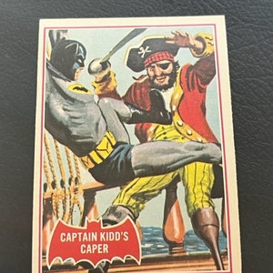 Könnte beinhalten: Eine Vintage-Batman-Sammelkarte mit einer farbenfrohen Illustration von Batman, der gegen Captain Kidd kämpft. Die Karte trägt den Text "Captain Kidd's Caper" in einem rot-weißen Fledermauslogo.