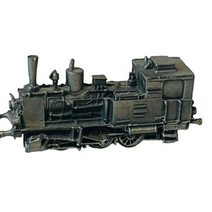 Puede incluir: Un modelo de locomotora de vapor vintage de peltre con acabado negro. El modelo está detallado con una chimenea, ruedas y una cabina.