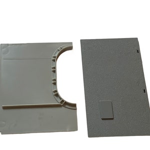 Pode incluir: Duas peças de plástico cinzento para um conjunto de comboios modelo. Uma peça é uma via recta com um pequeno rectângulo cinzento nela. A outra peça é uma via curva com um pequeno rectângulo cinzento nela.