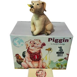 May include: A boxed figurine of a pig with a yellow leaf in its mouth. The box has a cartoon pig on it with a red ribbon that says "1". The box also has the text "Piggin' by David Corbridge for Collectible World Studios".