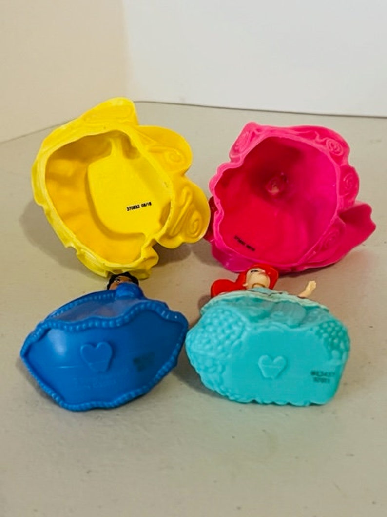 May include: Four plastic princess dolls with removable skirts. The dolls are Ariel, Belle, Cinderella, and Snow White. The skirts are yellow, pink, blue, and turquoise.