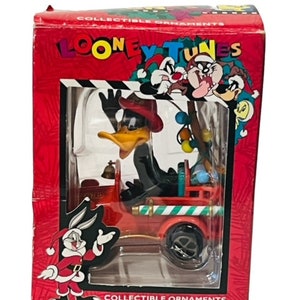 May include: A red and white Christmas ornament featuring a cartoon depiction of Tweety Bird driving a red fire truck. The ornament is part of a Looney Tunes collectible series.