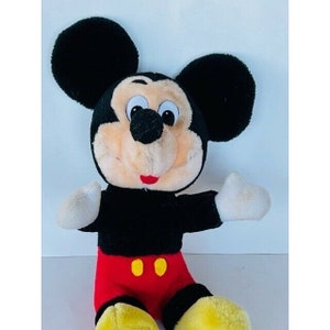 Puede incluir: Un juguete de peluche de Mickey Mouse con pelaje negro, orejas grandes, un atuendo rojo y amarillo y una gran sonrisa.