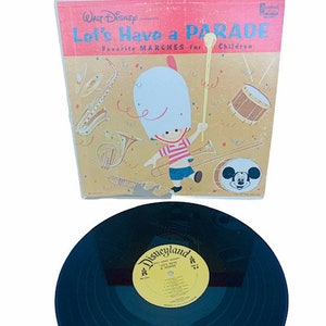 Könnte beinhalten: Eine Vintage-Schallplatte von Walt Disney Records mit einem roten und weißen Cover, das einen Comic-Charakter in einem Tambourmajor-Uniform und den Text "Let's Have a Parade Favorite Marches for Children" zeigt. Die Schallplatte ist schwarz und hat ein gelbes Etikett mit dem Text "Disneyland Let's Have a Parade".