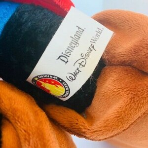 May include: A brown and black plush toy with a blue and red fabric patch on the head. The toy has a tag that reads "Disneyland. Walt Disney World. Original Disney Parks."