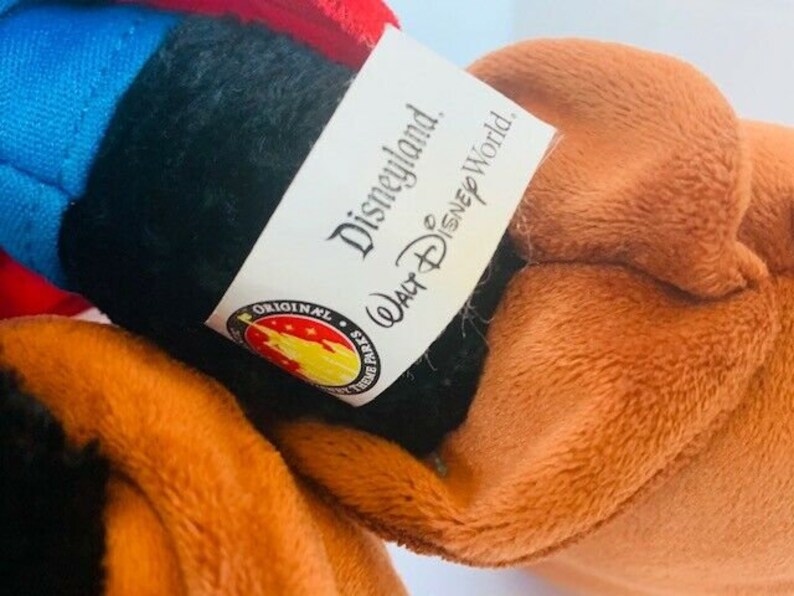 May include: A brown and black plush toy with a blue and red fabric patch on the head. The toy has a tag that reads "Disneyland. Walt Disney World. Original Disney Parks."