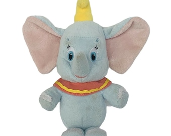 May include: A light blue plush toy elephant with large pink ears, a yellow hat, and a red and yellow collar.