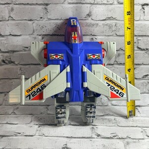 May include: A blue and light gray plastic toy jet with red accents and a translucent cockpit canopy. The wings feature yellow decals with the text GUARDIAN 7246. A yellow measuring tape is positioned vertically, showing a height of 8 inches.
