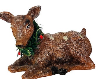 May include: A brown and white spotted deer figurine with a green holly wreath around its neck. The wreath has red berries and is partially in the deer's mouth.