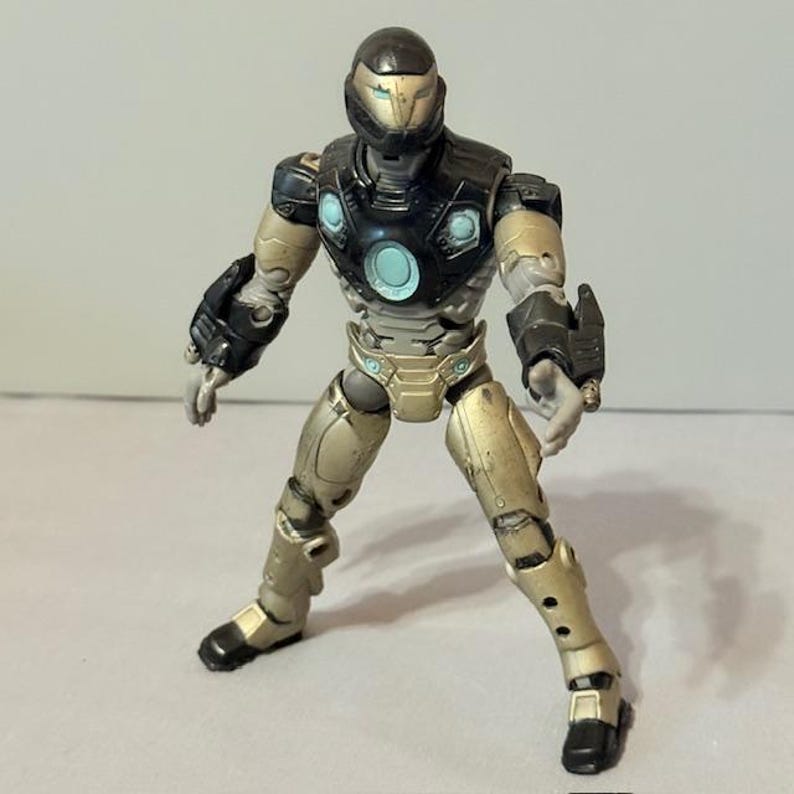 May include: A black and gold action figure of Iron Man in a futuristic suit. The figure has a black helmet with a blue visor and a gold chest plate. The figure is posed in a dynamic stance with one arm raised and the other extended.
