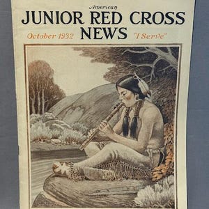 May include: Vintage American Junior Red Cross News magazine cover from October 1932. The cover features an illustration of a person playing a flute near a river. The magazine title is in bold black letters, with the words "I Serve" below.