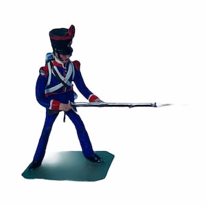 May include: A toy soldier figurine in a blue uniform with red accents, holding a rifle and standing on a green base.