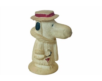 Può includere: Statuetta vintage di un personaggio dei cartoni animati con un lungo muso, che indossa un cappello con una fascia rossa, una sciarpa e un cappotto. La statuetta è dipinta in bianco sporco con accenti neri e rossi. Il personaggio tiene in mano una pipa.