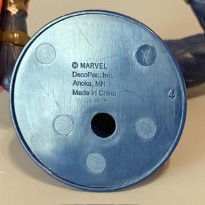 May include: Blue plastic base of a figurine with the text "&copy; MARVEL DecoPac, Inc. Anoka, MN Made in China 387301 05/16" printed on it.